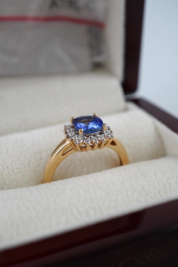 A modern 18ct gold, tanzanite and diamond cluster set ring, with AnchorCert report estimating the cushion cut tanzanite to weigh 0.90ct, size O, gross weight 3.5 grams. Condition - good